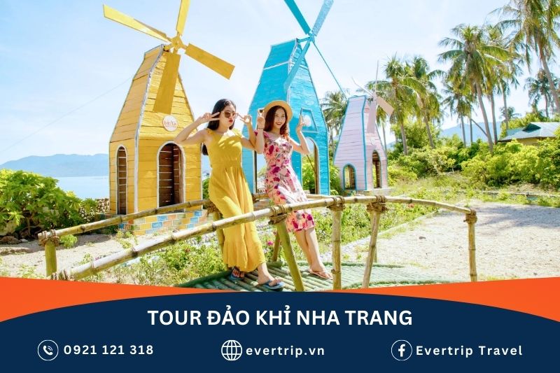 2 du khách đi tour chụp ảnh trên bãi biển đảo khỉ nha trang, phía sau là 2 cối xây gió màu vàng và xanh